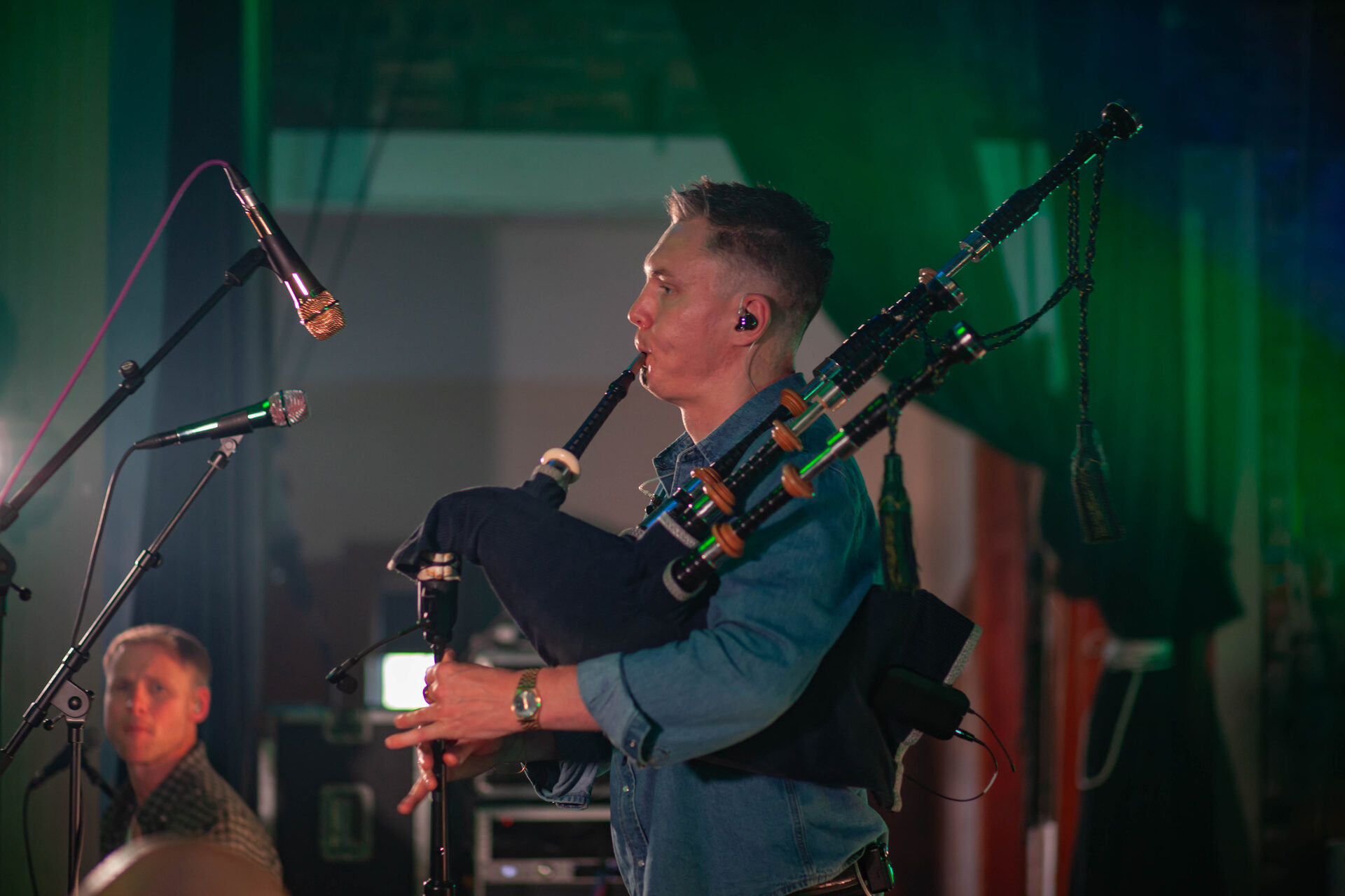 Piper playing the Highland bagpipes under green stage light