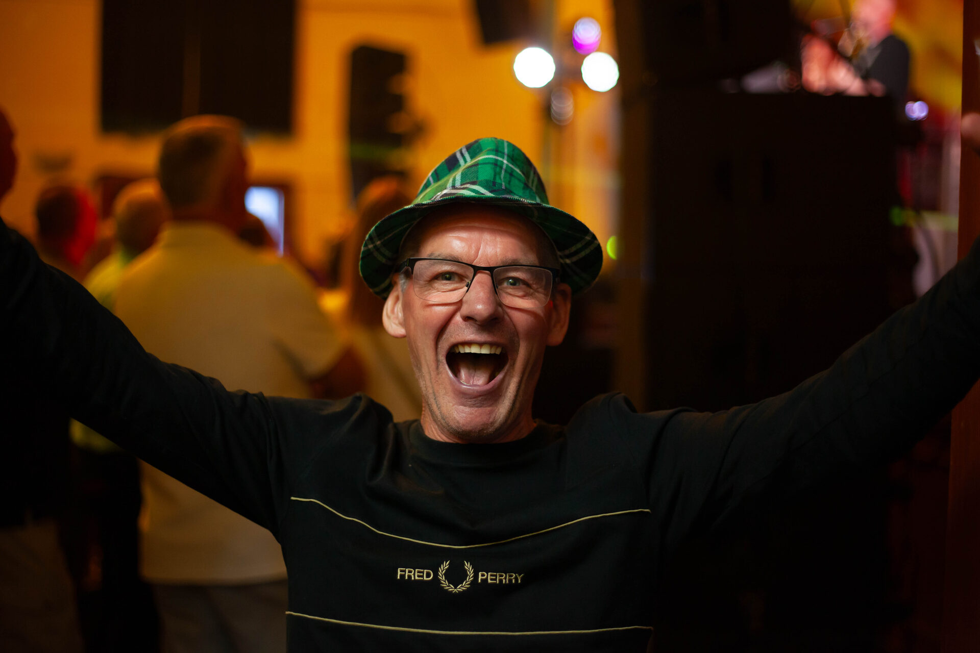 Festival-goer in a tartan hat laughing with his arms wide