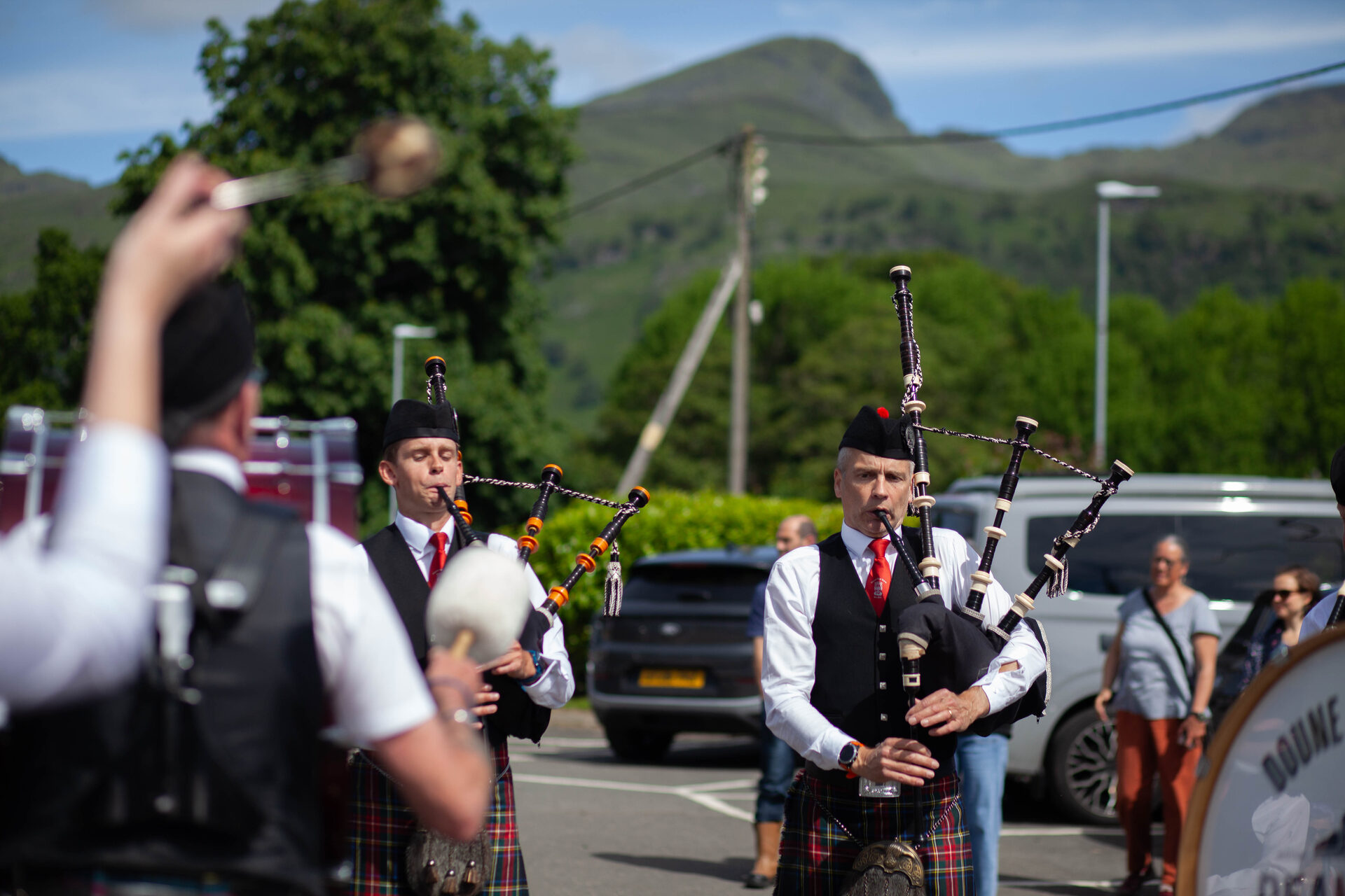 Two pipers in full Highland dress with a sunlit hill behind