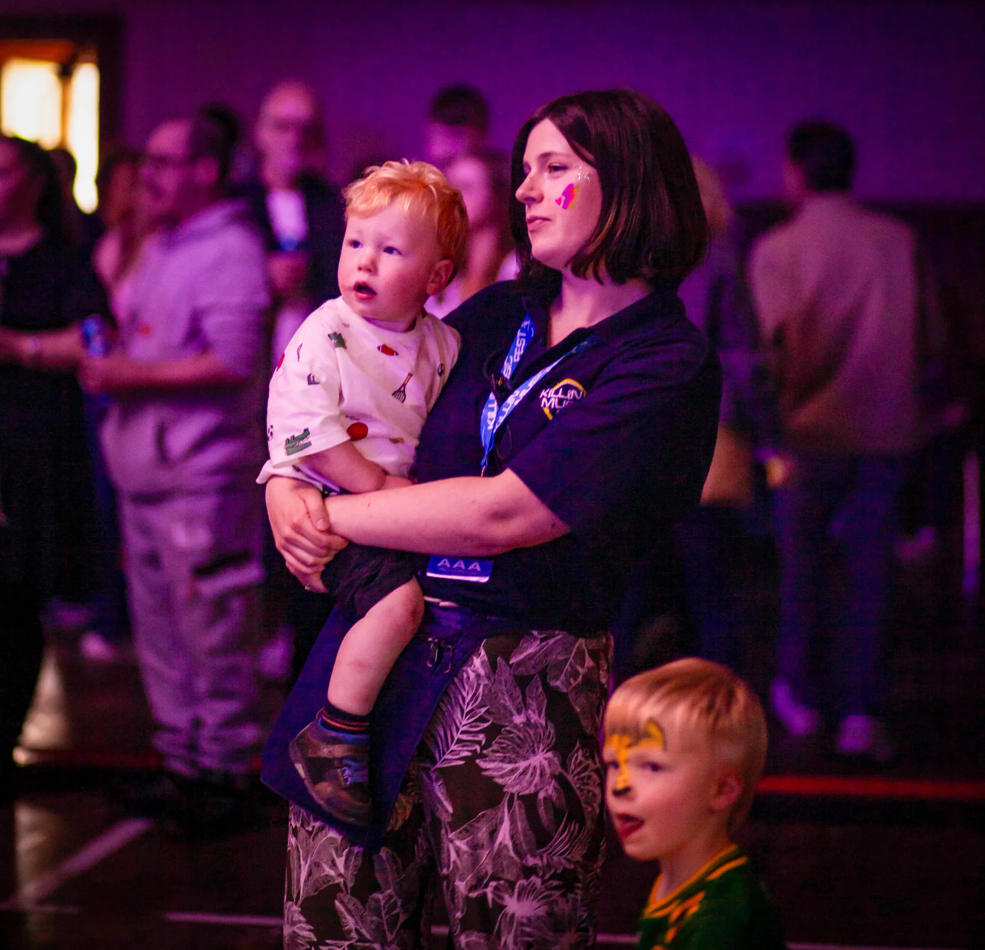A crew volunteer and a wee fan in a festival hoodie watching the stage together