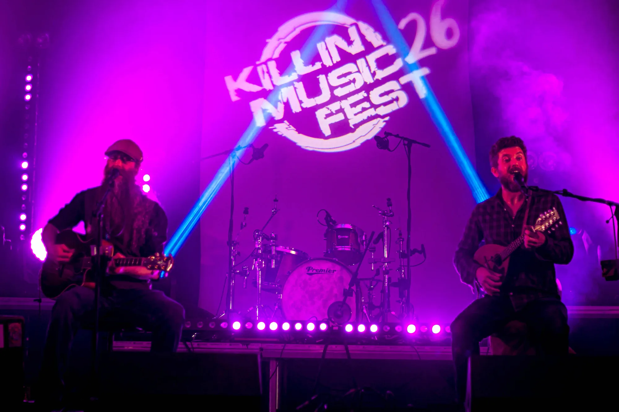 Mad Ferret Band on guitar and mandolin under purple light with the festival logo behind